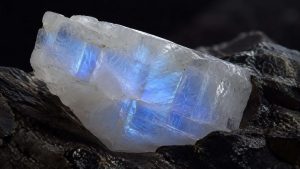Muestra de adularia blanca con un destello azulado sobre roca oscura