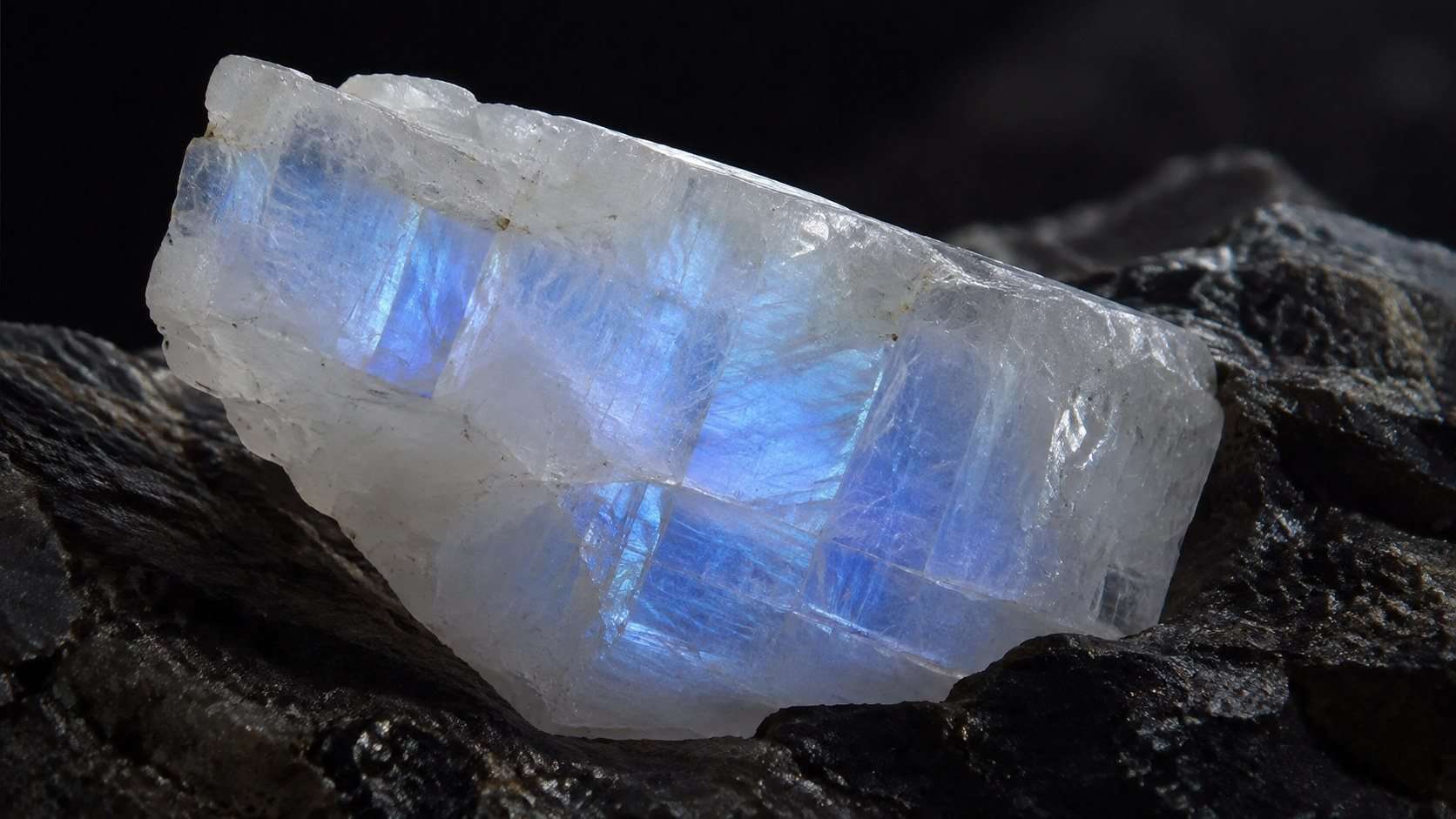 Adularia: cómo identificar la piedra lunar sin confundirla con imitaciones — Imagen 1 Muestra de adularia blanca con un destello azulado sobre roca oscura